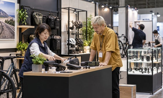 自転車用品の展示ブースでカウンターと展示備品を確認するスタッフ｜レンタル1番ドットコム